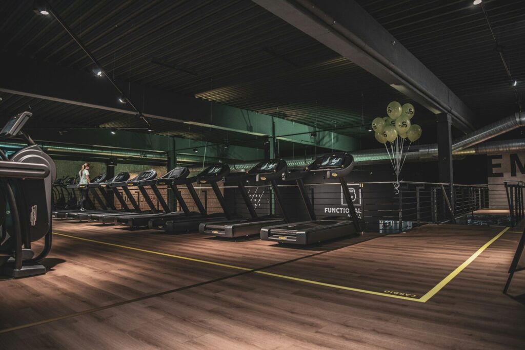 A row of treadmills in a gym with wooden floors and green balloons